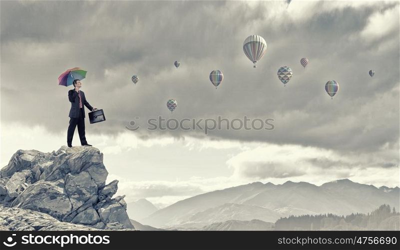 Man with colorful umbrella. Businessman with umbrella and suitcase standing on mountain top