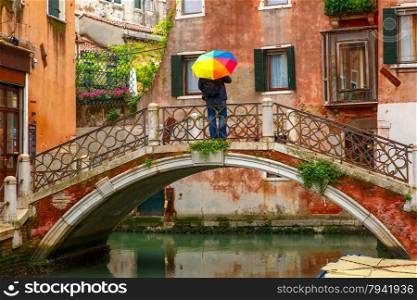 Man with colorful umbrella on picturesque bridge over Venetian canals on a rainy day, Italy