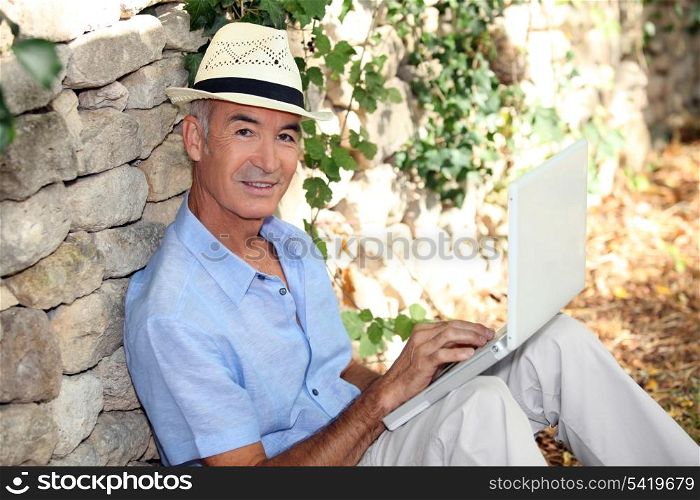 Man with computer leaning on stone wall
