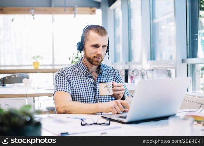 man with cup headsetworking laptop