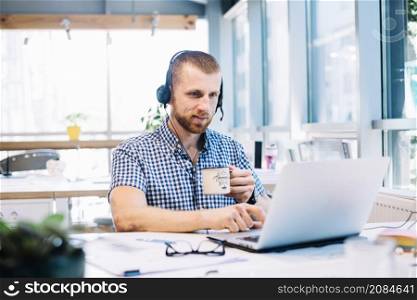 man with cup headsetworking laptop
