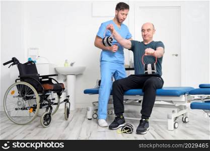 Man with disability doing recovery exercise with dumbbell. Man with Ataxy in recovery support therapy physiotherapy healthcare system. High quality photo.. Man with disability doing recovery exercise with dumbbell. Man with Ataxy in recovery support therapy physiotherapy healthcare system.