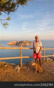 Man with dog in front of landscape with Les Medes islands in sunset at the horizon