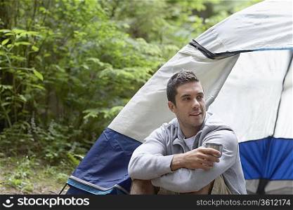 Man with drink, sitting by tent