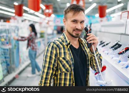 Man with electric shaving machine, couple in supermarket. Male and female customers on family shopping. Man and woman purchasing goods for the house
