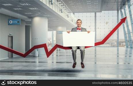 Man with empty banner. Young businessman sitting on arrow holding white blank banner in modern office