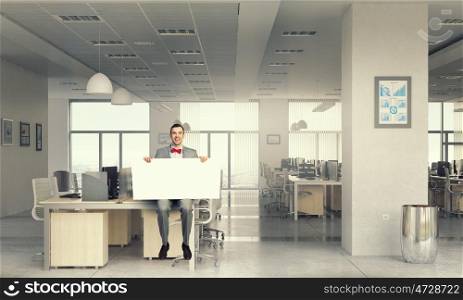Man with empty banner. Young businessman sitting on table holding white blank banner in modern office