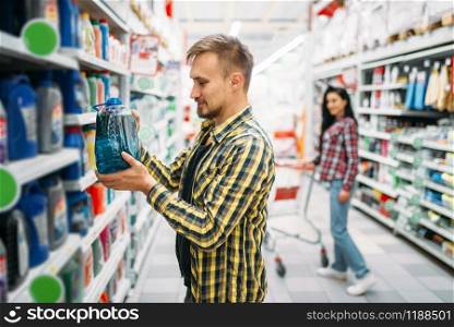Man with engine oil canisters, couple in supermarket. Male and female customers on family shopping. Man and woman purchasing, department of goods for cars. Man with engine oil, couple in supermarket