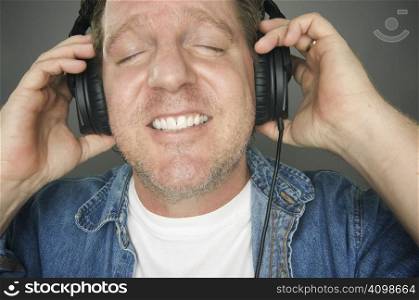 Man with Eyes Shut Wearing Headphones Enjoying His Music on a Grey Background.