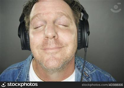 Man with Eyes Shut Wearing Headphones Enjoying His Music on a Grey Background.