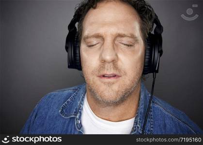 Man with Eyes Shut Wearing Headphones Enjoying His Music on a Grey Background.. Man With Headphones