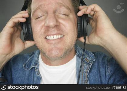Man with Eyes Shut Wearing Headphones Enjoying His Music on a Grey Background.. Man Wearing Headphones