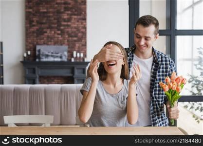 man with flowers surprising cheerful woman