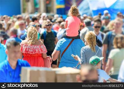 Man with girl in crowd of people walking on city street 