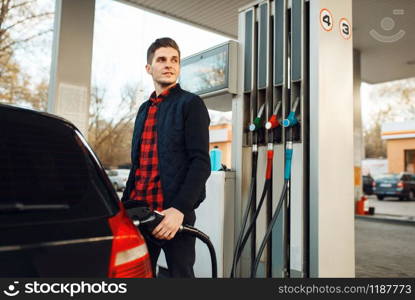 Man with gun fuels vehicle on gas station, bottom view, fuel filling. Petrol fueling, gasoline or diesel refuel service. Man fuels vehicle on gas station, bottom view