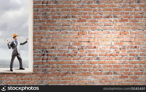 Man with hammer. Businessman in helmet hammering nail in brick wall