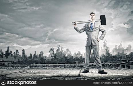 Man with hammer. Young businessman with hammer and ruins at background