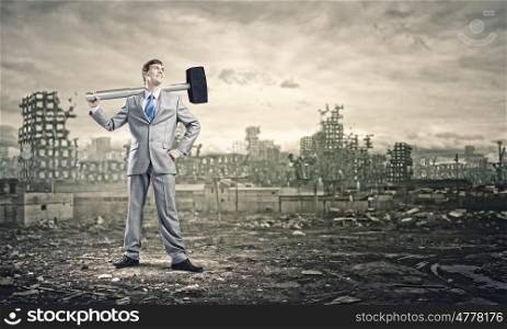 Man with hammer. Young businessman with hammer and ruins at background