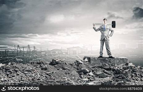 Man with hammer. Young businessman with hammer standing on ruins