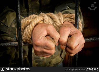 Man with hands tied up with rope behind the bars