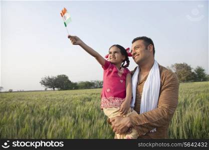 Man with his daughter holding Indian flag in an agricultural field