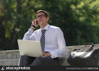 Man with laptop calling by phone at summer park on bright day