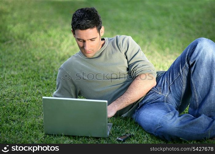 Man with laptop laying in field
