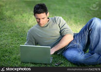 Man with laptop laying in field