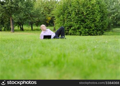 man with laptop lying on green grass in the park