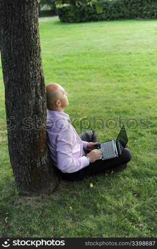 man with laptop sitting near a tree in the park