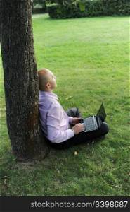 man with laptop sitting near a tree in the park