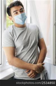 man with medical mask home during pandemic sitting window