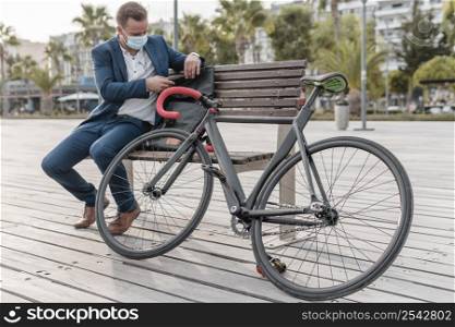 man with medical mask sitting bench his bike