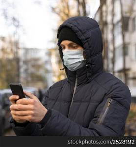 man with medical mask using smartphone outdoors