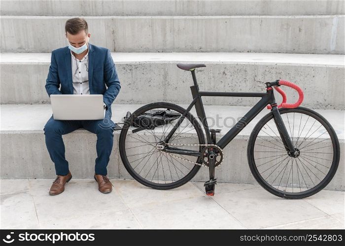 man with medical mask working laptop bike