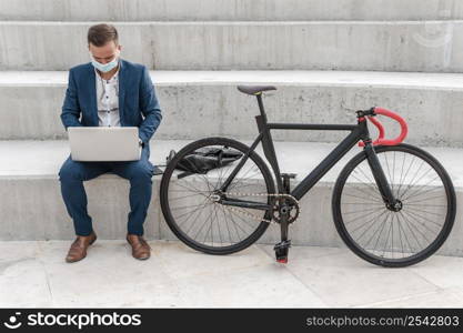 man with medical mask working laptop bike