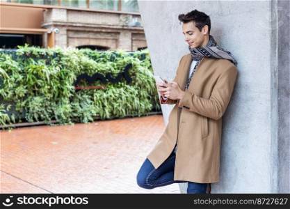 Man with mobile phone and autumn styling leaning on outdoor wall
