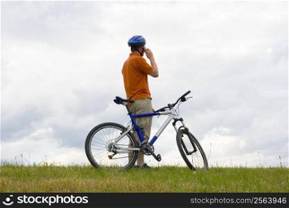 Man with mountain bike in a meadow talking on mobilel phone