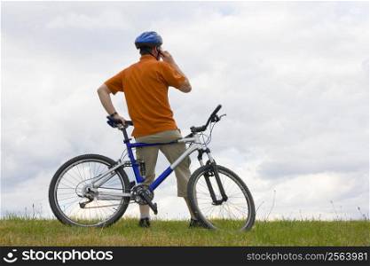 Man with mountain bike on a meadow talking on cell phone