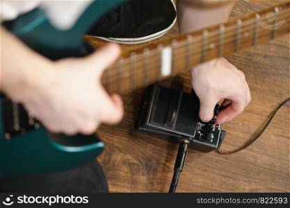 Man with musical instrument setting up guitar audio stomp box effects and cables in music studio. Man adjusting guitar effects pedal