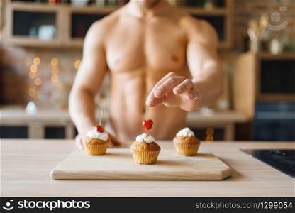 Man with naked body cooking cakes with cherry on the kitchen. Nude male person preparing breakfast at home, food preparation without clothes