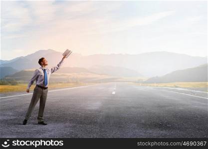 Man with opened book. Young businessman on road reaching hand with opened book