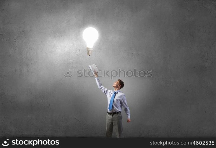 Man with opened book. Young screaming businessman on pile reaching hand with opened book and light bulb flying out