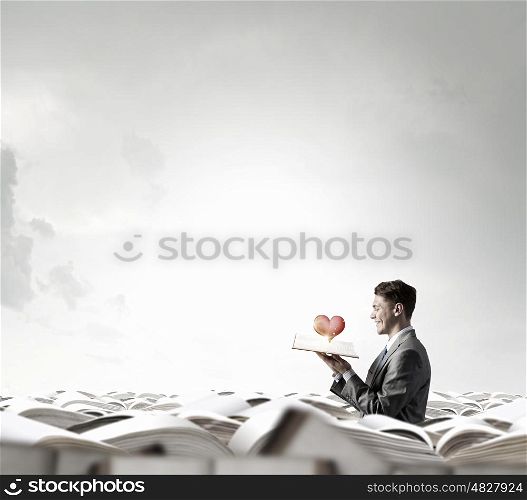 Man with opened book. Young shocked businessman with opened book in hand and red heart on pages