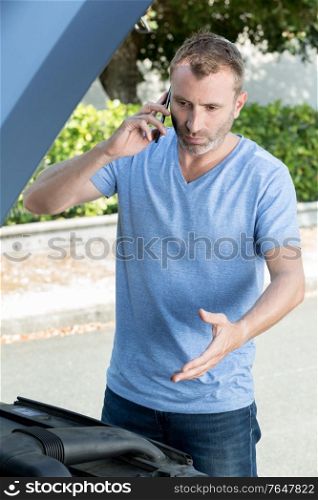 man with opened hood calling for help on cellphone
