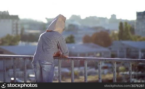Man with paper bag over head and sunglasses dancing against a city scape