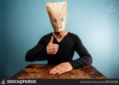 Man with paper bag over his head giving thumbs up