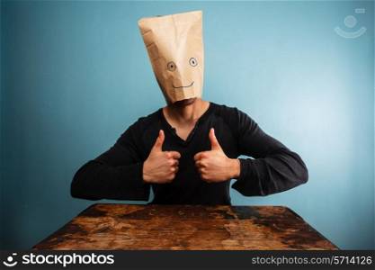 Man with paper bag over his head giving two thumbs up