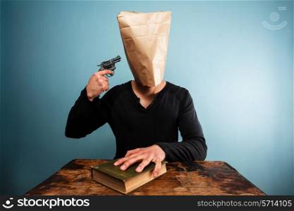Man with paper bag over his head pointing gun at himself