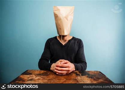 Man with paper bag over his head sitting at desk